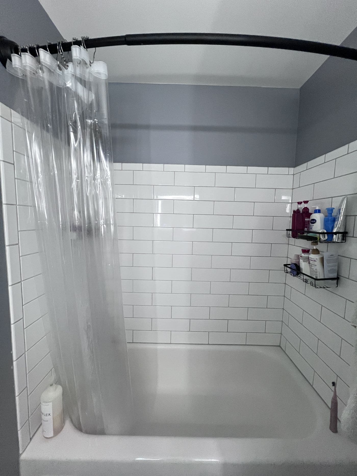 The Amherst bathroom before the remodel: a dated tub behind a plastic shower curtain