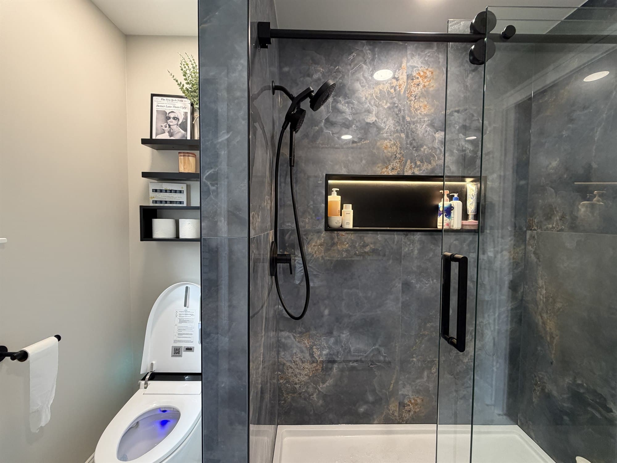 Wide view of the finished bathroom showing the shower niche, black fixtures and floating shelves
